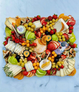 Colorful charcuterie board with meats, cheeses, fruits, olives, pickles, and nuts.